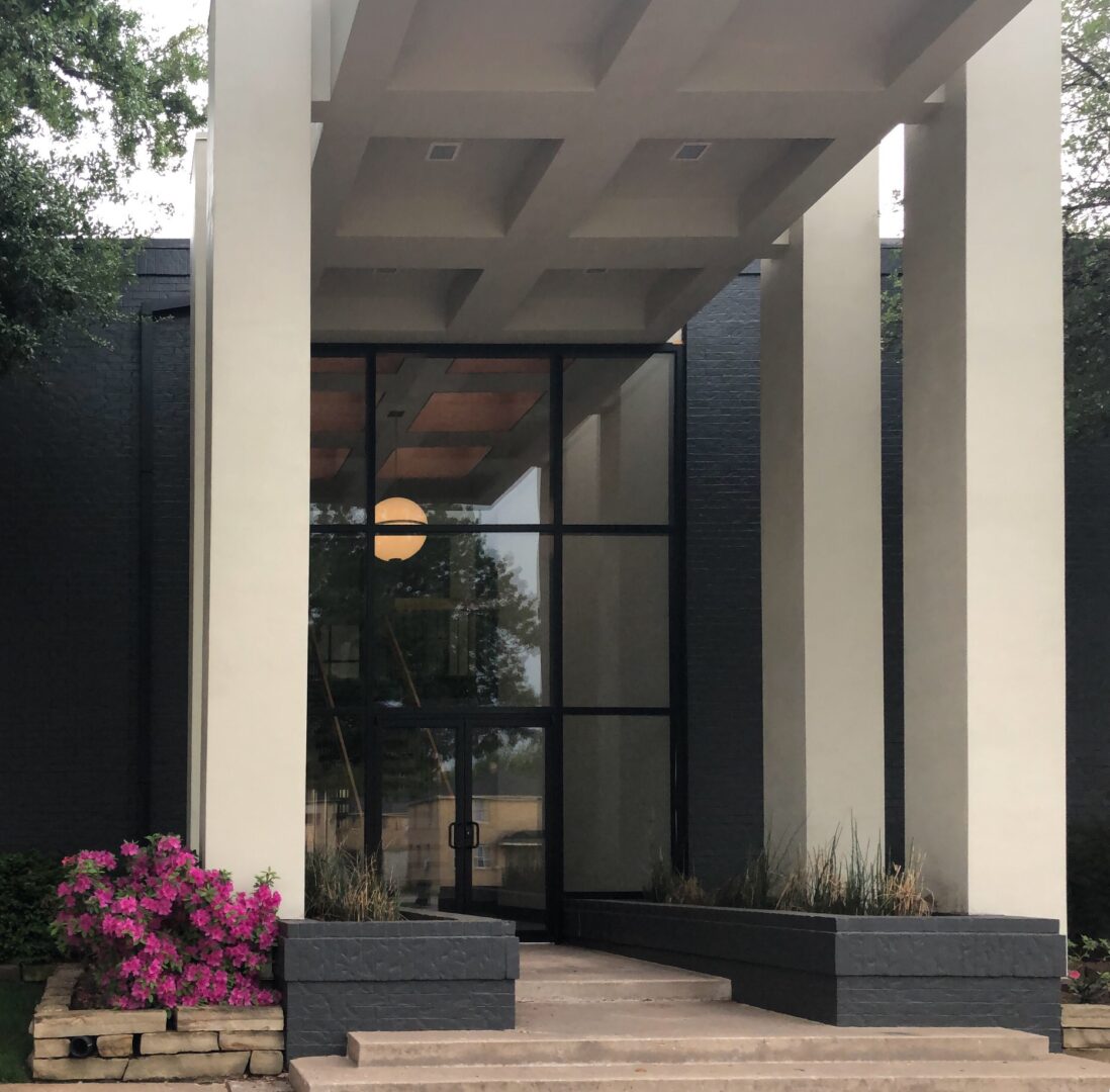 A building with columns and plants in front of it.