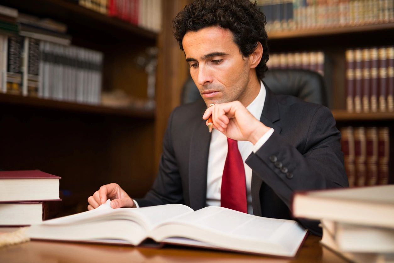 A man in suit and tie sitting at desk with open book.